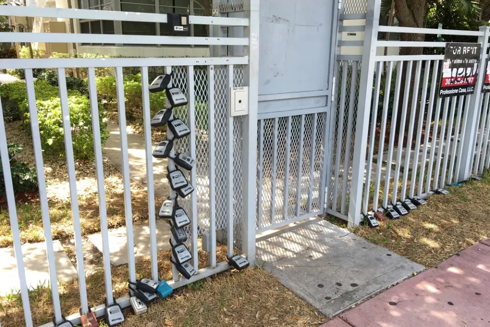 Gate in front of Miami Beach apartment building with many lock boxes for short-term renter access